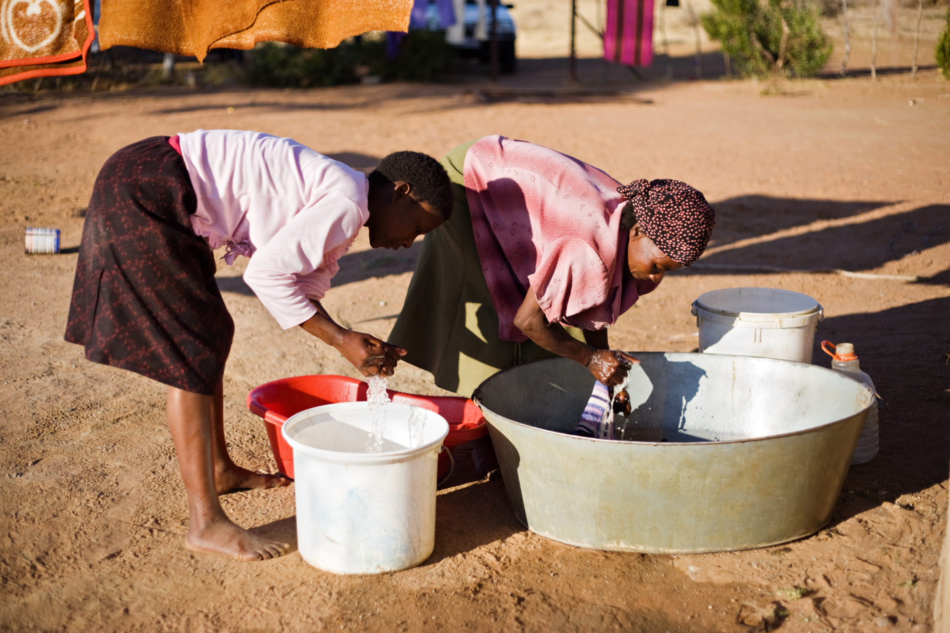 Two kids washing their hands using water collected in buckets