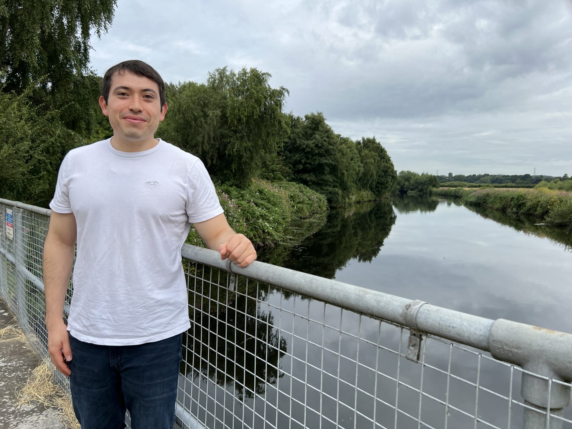 researcher standing beside a river and leaning on a railing.