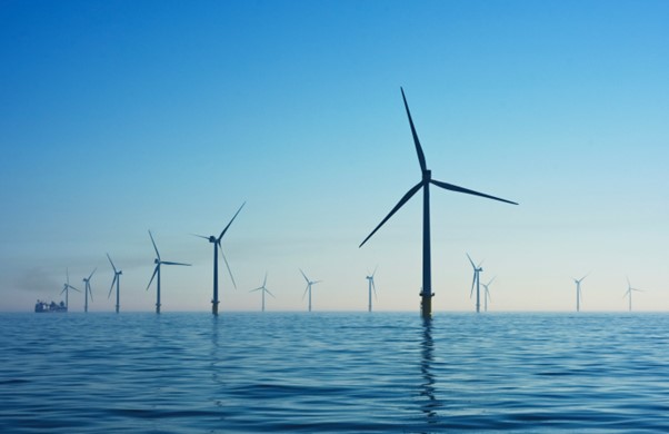 A wind farm in the ocean showing blue sky and peaceful waters